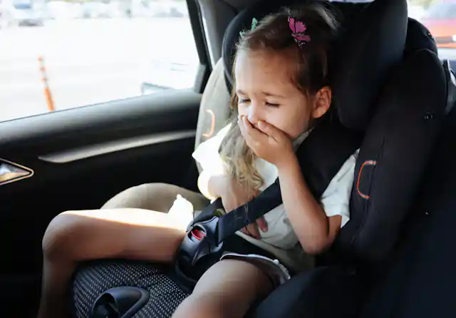 girl in carseat covers her mouth