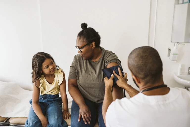 Mother talking to daughter in exam room, getting blood pressure taken