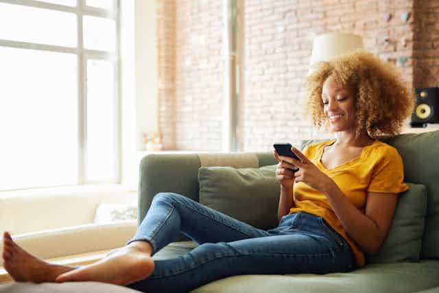 Young woman relaxes on sofa and looks at cell phone