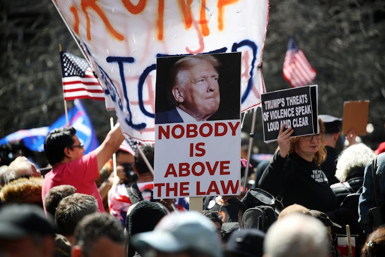 A crowd of people hold American flags and signs that say things like 'no one is above the law.'