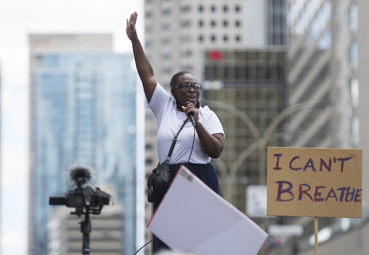 A woman seen with a microphone in front of sign 'I can't breathe.'