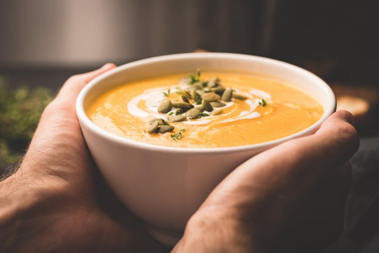 hands cradle a bowl of pumpkin soup