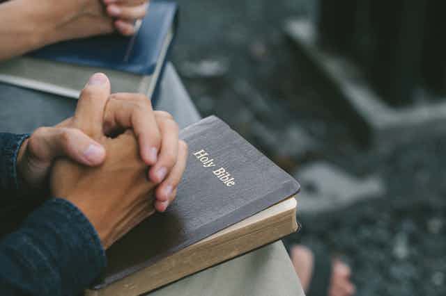 Person with hands folded over a Holy Bible