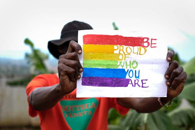 A man in Uganda holding a rainbow sign saying 'be proud of who you are'