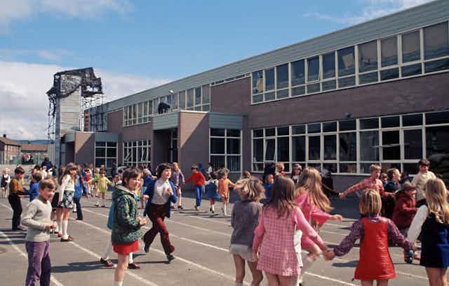 Landscape photo of children playing in playground with scaffolded tower attached to school behind