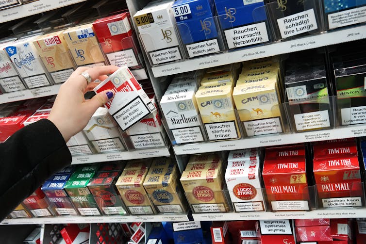 Someone reaches for a pack of cigarettes from a large shop display.
