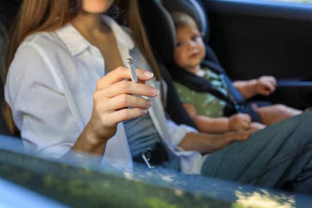 Mujer fumando en un coche con un niño pequeño al lado.
