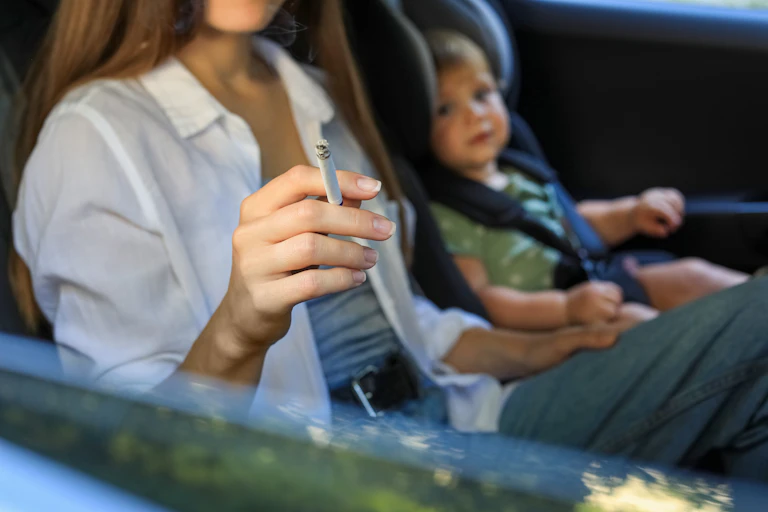 Mujer fumando en un coche con un niño pequeño al lado.
