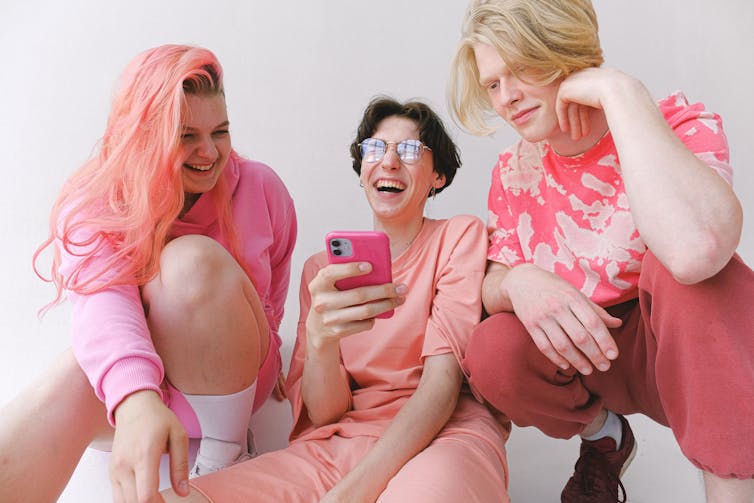 Group of friends, wearing pink, looking at a phone.