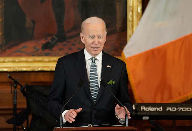 Joe Biden speaks at a podium in front of an Irish flag