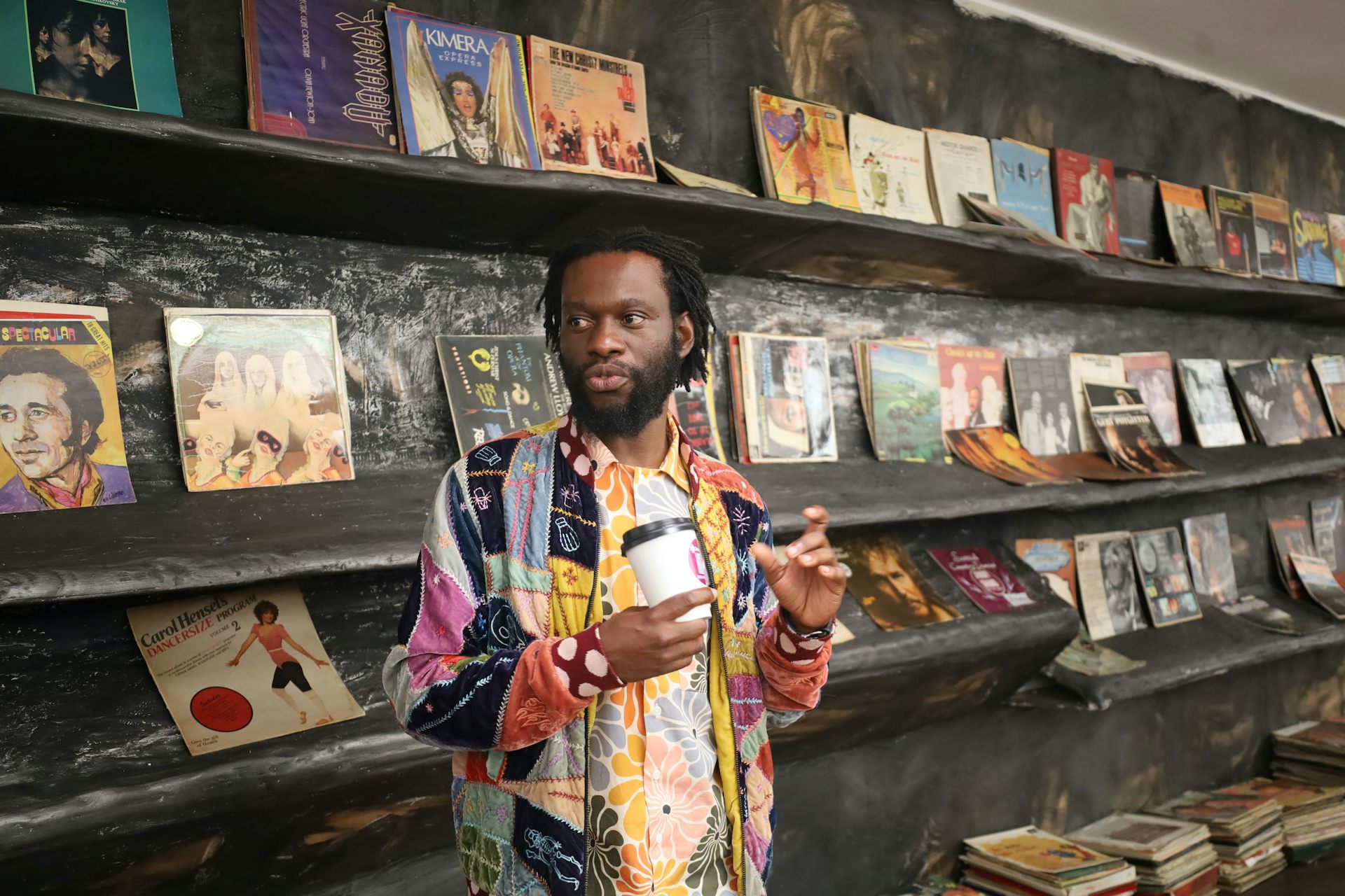 Long brown shelves display old LP records while stacks of records sit beneath it on the floor.