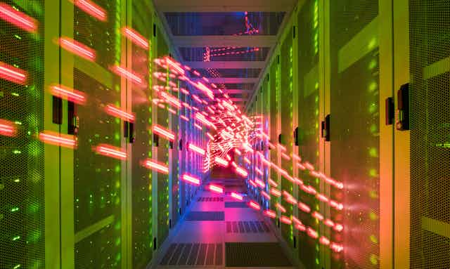 A corridor in a data centre with servers in cabinets on either side and red lights flowing between them.