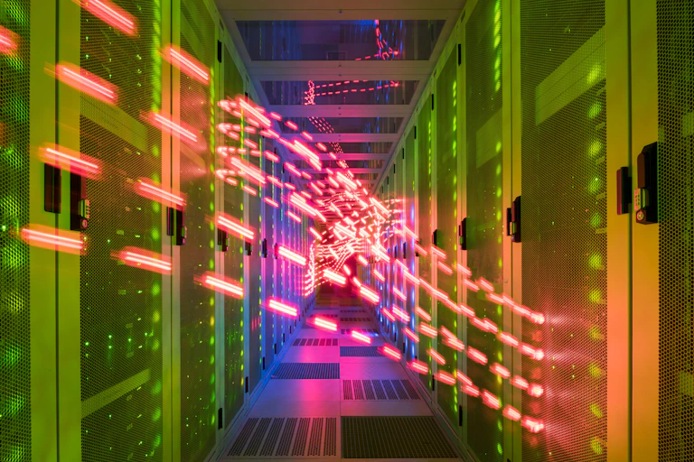 A corridor in a data centre with servers in cabinets on either side and red lights flowing between them.
