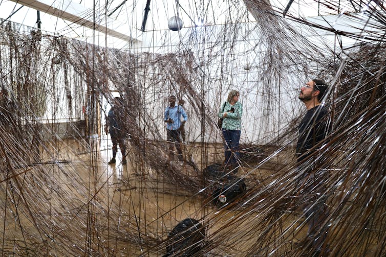 A man stands within a maze of tape strung from a suspended frame.