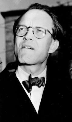 A man wearing glasses and a bow tie squints.
