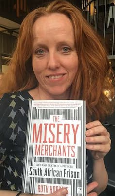 A woman with long hair smiles slightly as she holds a book with the title The Misery Merchants.