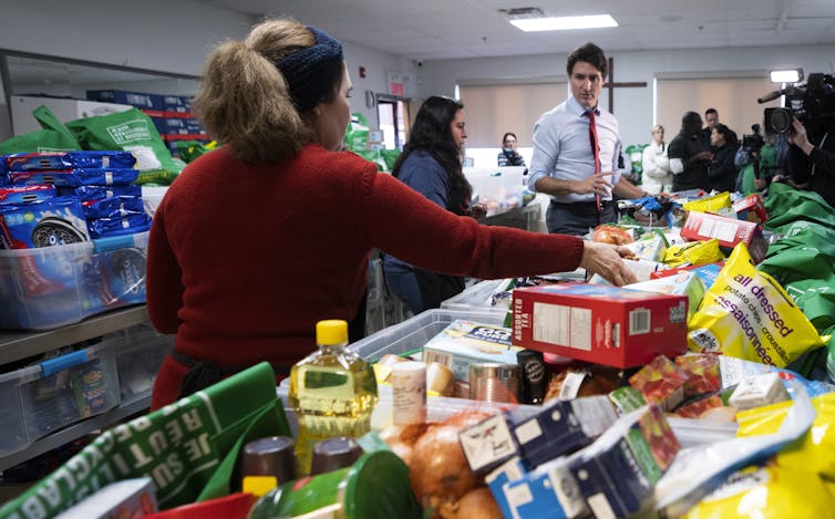 A dark-haired man in a shirt and tie loads food baskets with goods.