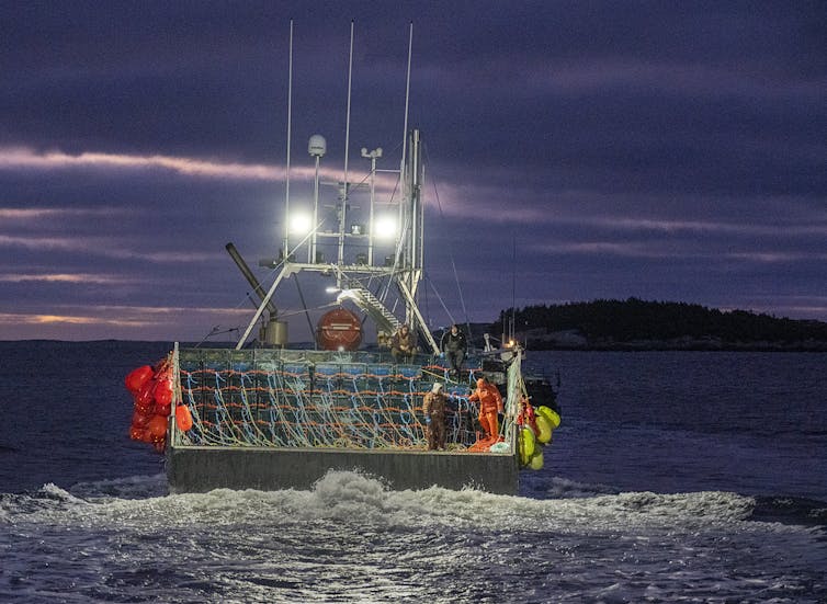 A fishing boat with visible lobster pots and buoys heads out to the open sea at dawn.