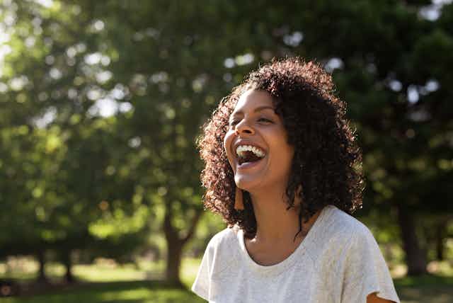 A woman laughing outdoors.