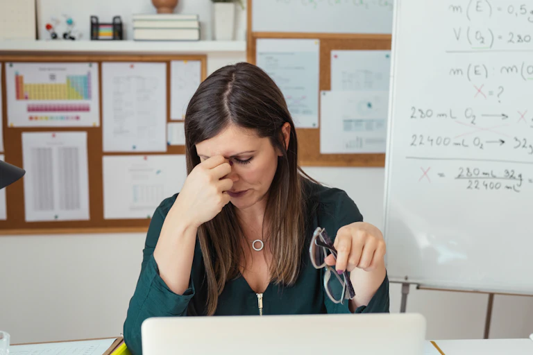 Stressed teacher takes off glasses in classroom