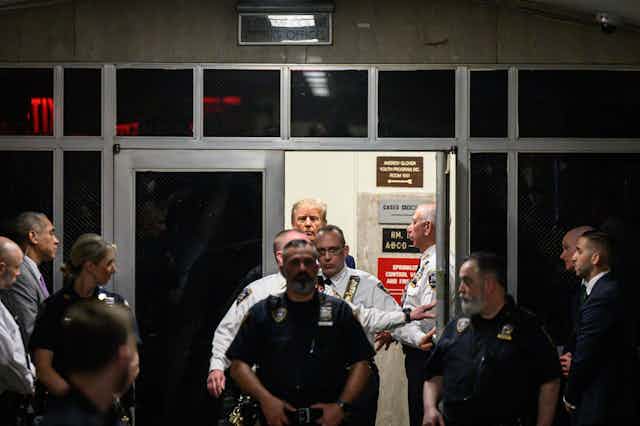 A row of men, some of them wearing police uniforms, all through an open door in a dimly lit room. 