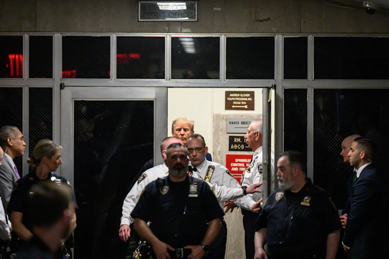 A row of men, some of them wearing police uniforms, all through an open door in a dimly lit room.
