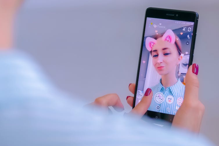 A young woman uses a filter to add pink ears to her photo.