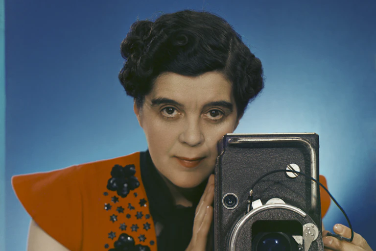 A self portrait of Yveonde. She wears a red shoulder padded top and holds a large camera.