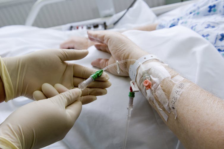 A person holding an IV line with a patient's arm.