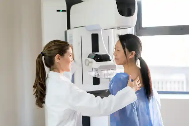 Female doctor talking to her patient and adjusting her position to do a mammogram.