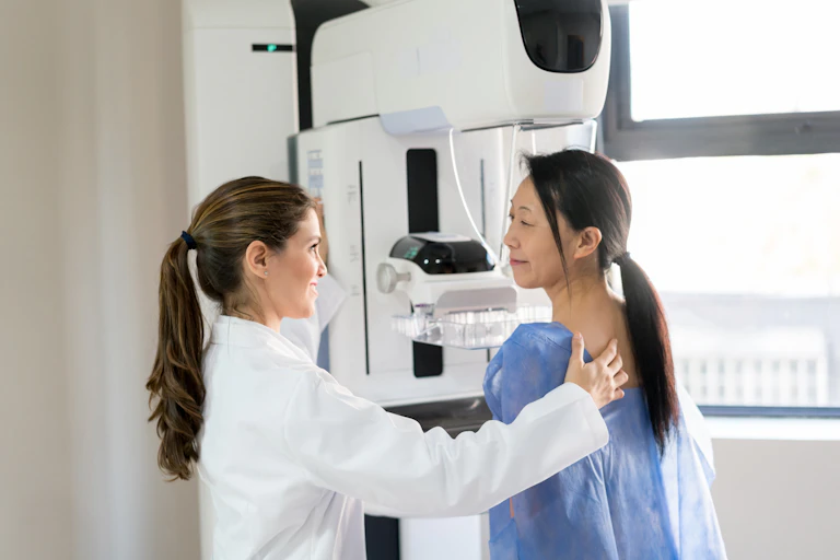 Female doctor talking to her patient and adjusting her position to do a mammogram.