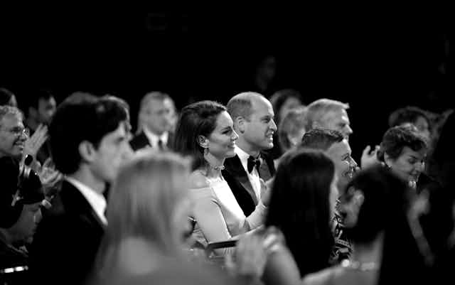 Prince Harry sitting in a crowd wearing a suit and tie.