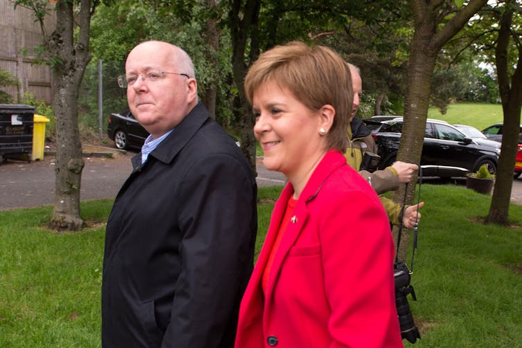 Nicola Sturgeon dressed in a red suit with her husband Peter Murrell in black.