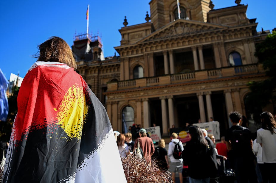 Protester wears Aboriginal flag in front of buildingof 