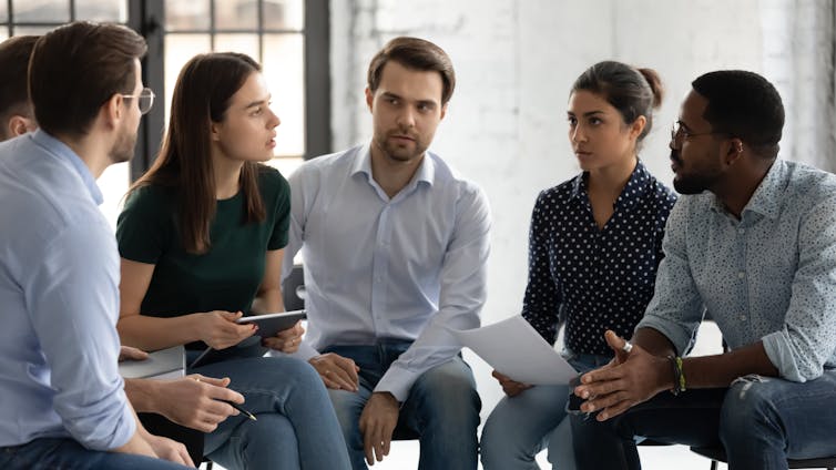 Young professionals company employees diverse staff members gather together sit on chairs brainstorming solving working moments having dispute express opinion point of view.