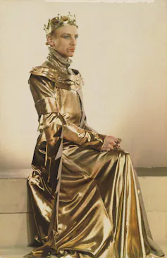 John Gielgud poses in an all-gold dress with a crown, looking to the right of the photograph. The colour is highly saturated.