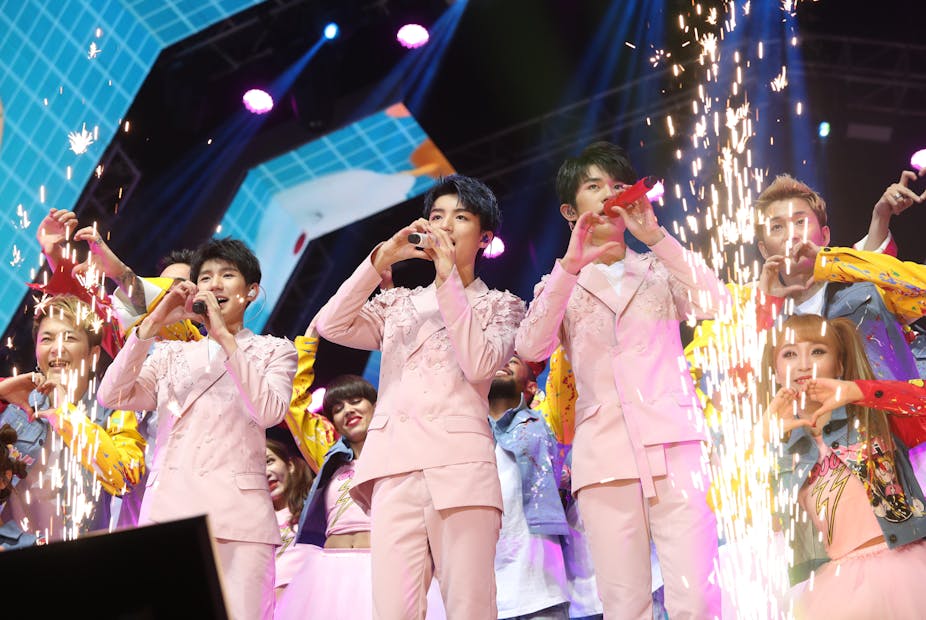 Chinese boy band TFBoys performing in pink suits surrounded by sparkler flares. 