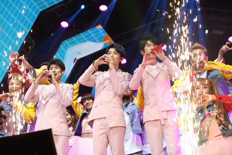 Chinese boy band TFBoys performing in pink suits surrounded by sparkler flares.