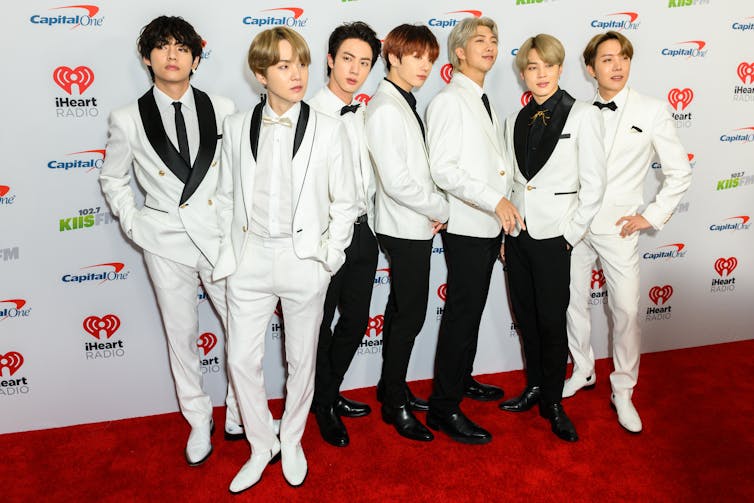 All seven members of BTS pose on a red carpet in white suits.