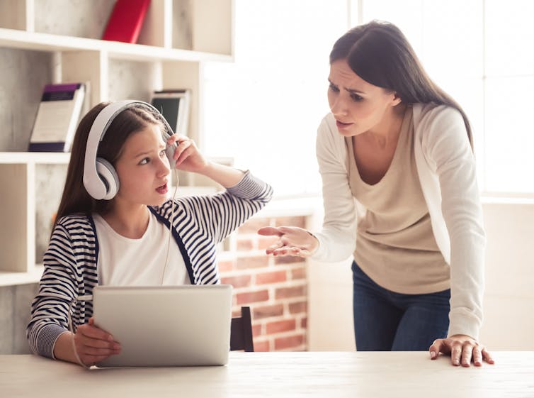Mother trying to talk to her daughter who is on tablet with headphones