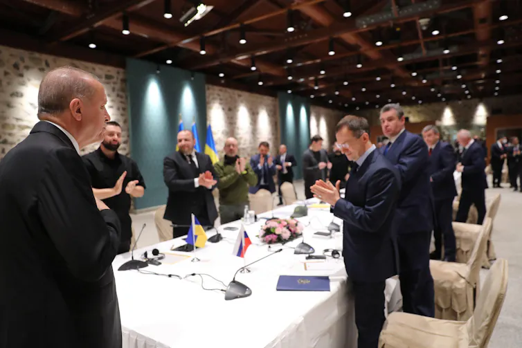 A group of men stand around a table applauding Turkish president Recep Tayyip Erdoğan