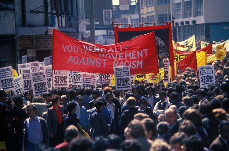 A colour photograph of protestors against racism with red banners.