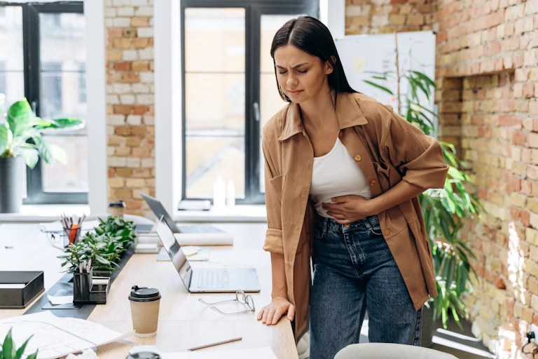 Woman clutches stomach while working in an office.
