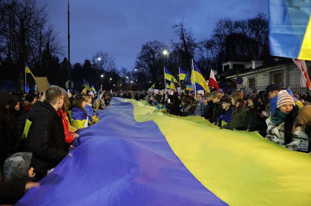People holding a massive Ukrainian flag stretching back along a road.