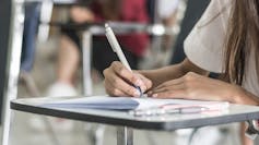 A hand seen writing a test on a classroom desk.