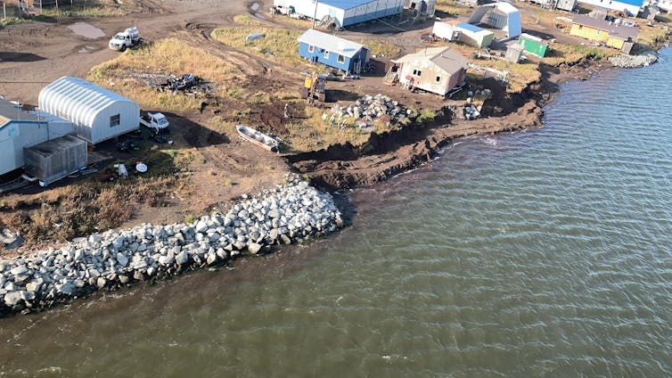 An aerial photo of the coast showing a rock border on the coast ending and erosion clearly evident beyond it.