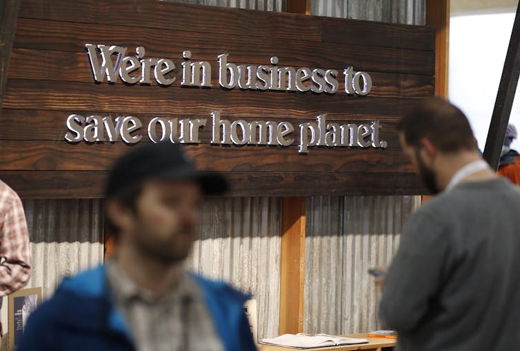 People pass by a wooden sign that says 'We're in business to save our home planet.'