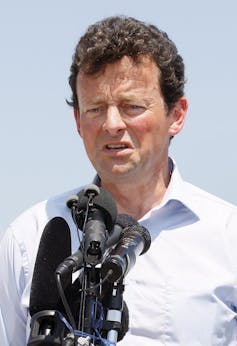 A middle-aged white man with short, curly brown hair speaks into a microphone.