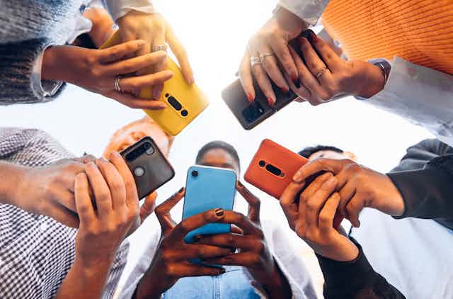 Five people holding different coloured smartphones, shot from below so the phones obscure their faces