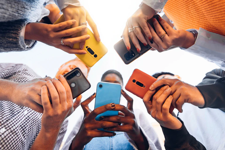 Five people holding different coloured smartphones, shot from below so the phones obscure their faces